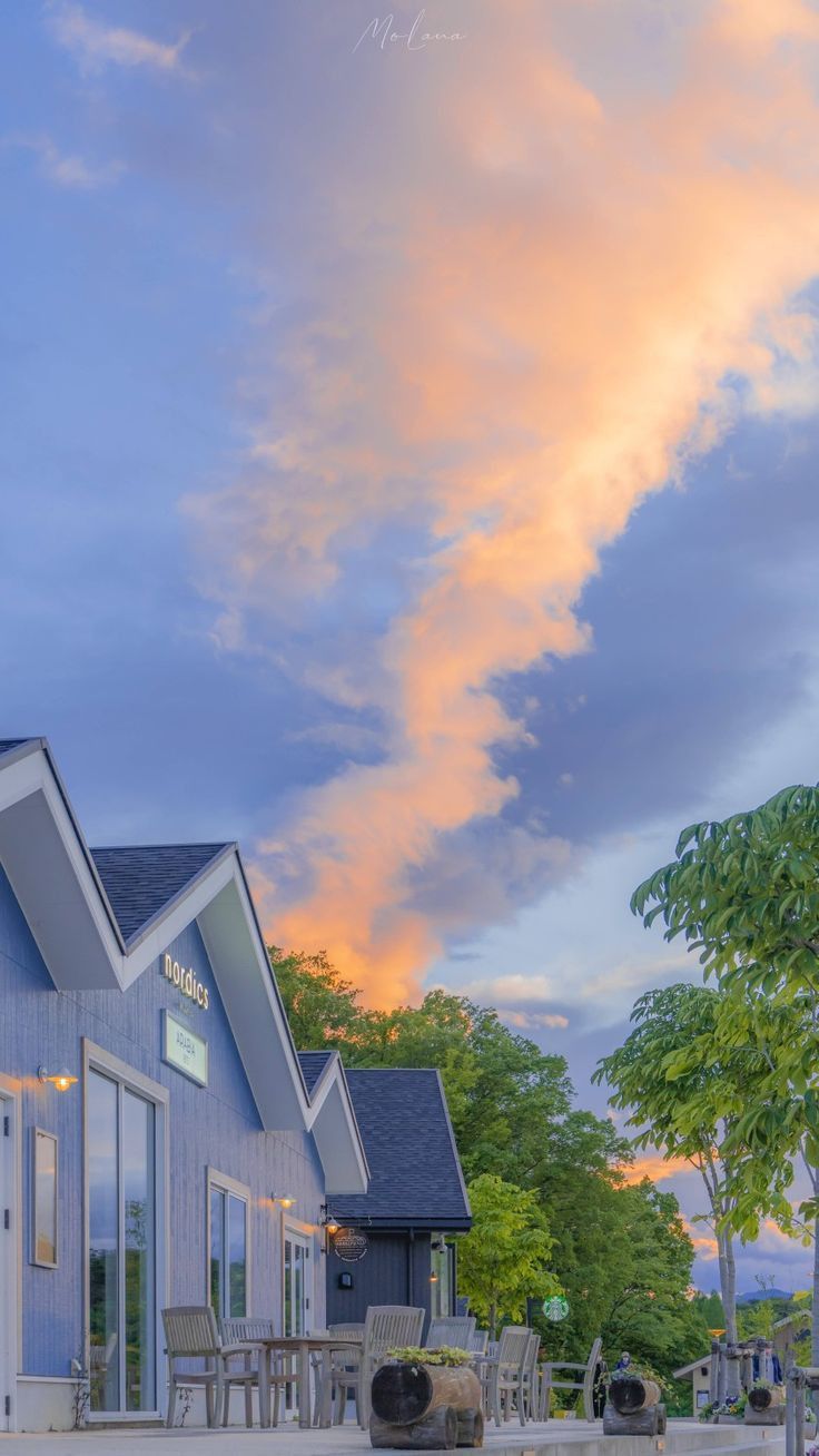 Orange sunset clouds over a quiet suburban street with a house and trees.