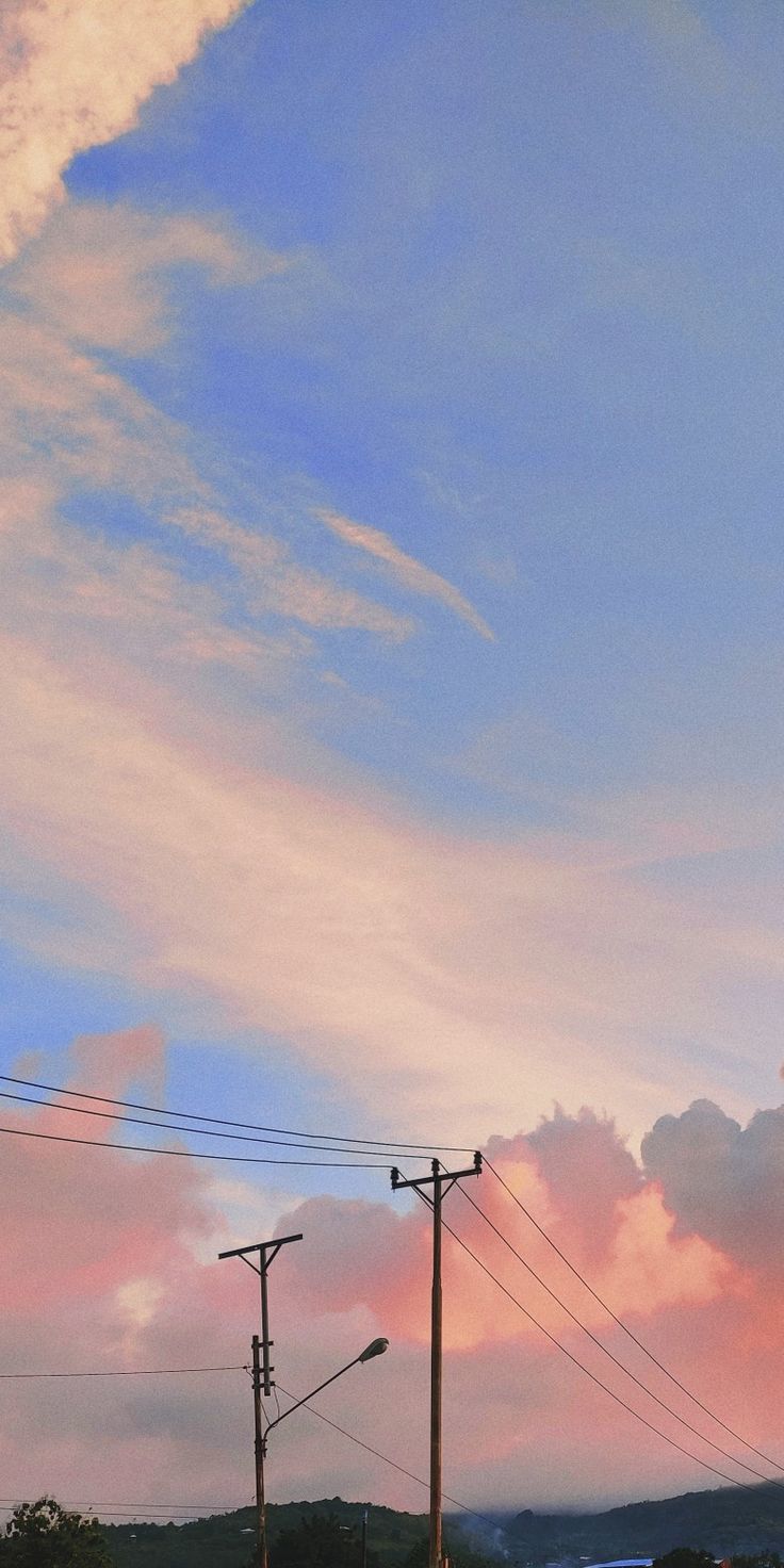 Power lines and poles silhouetted against pink sunset clouds on a pale blue sky.