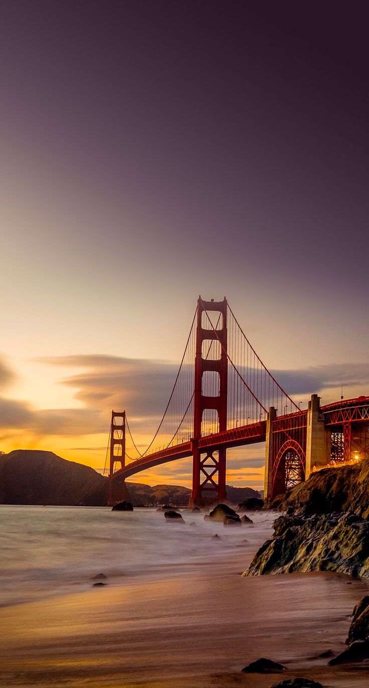 The Golden Gate Bridge at sunset, seen from a rocky beach.