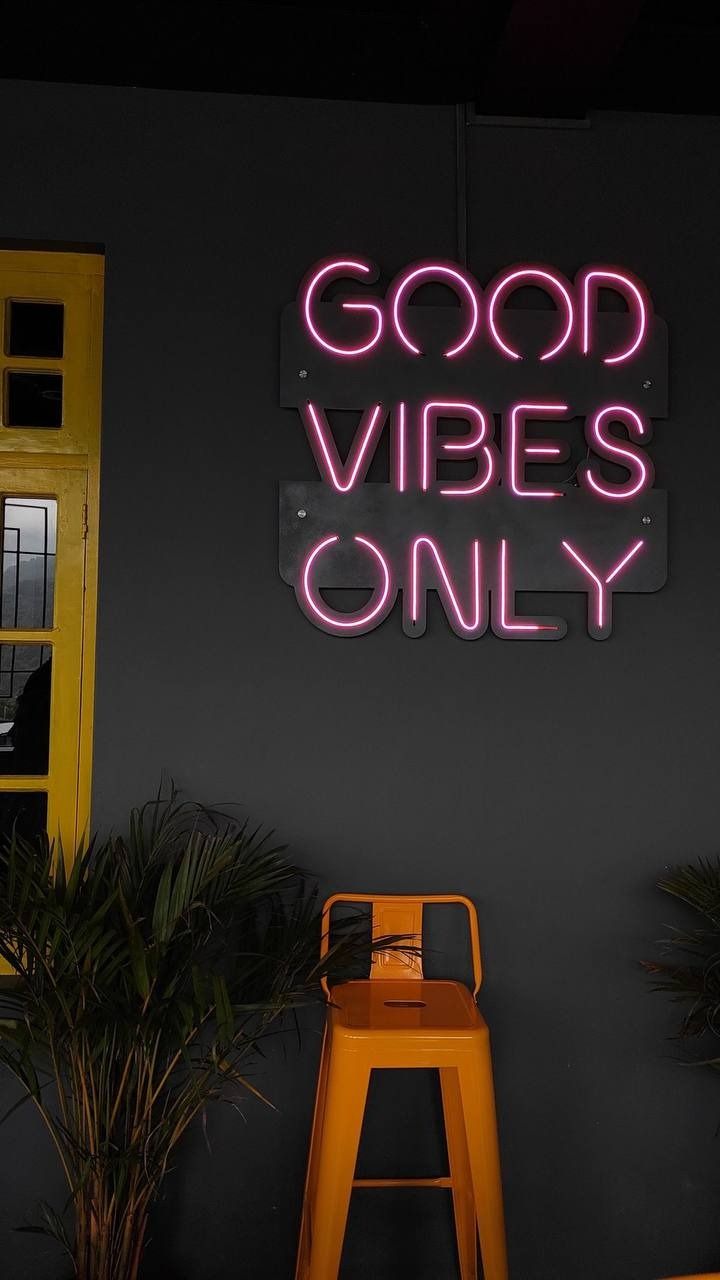 "Good vibes only" in pink neon above an orange bar stool against a dark wall.