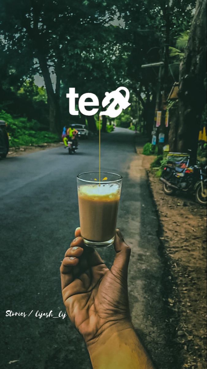 "Tea" in white above a hand holding a glass of milky tea on a green street.