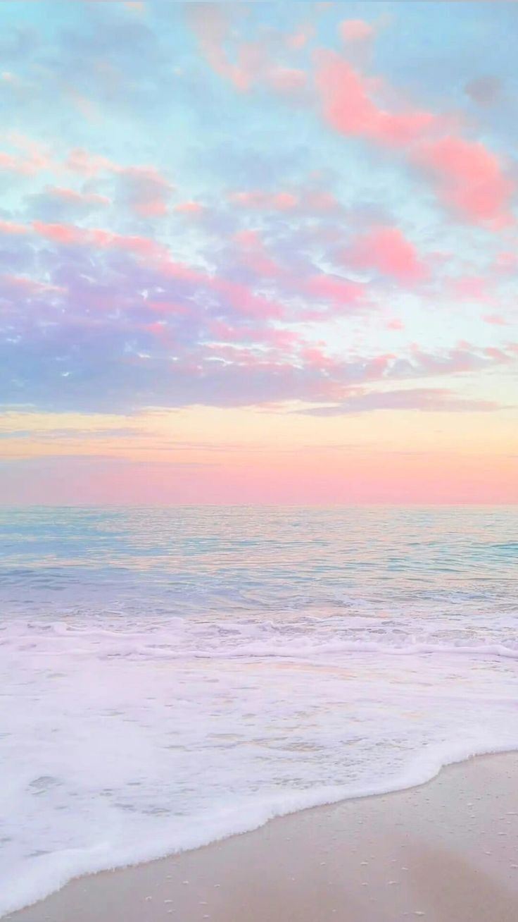 Pink and blue sunset clouds above gentle waves on a pale beach.