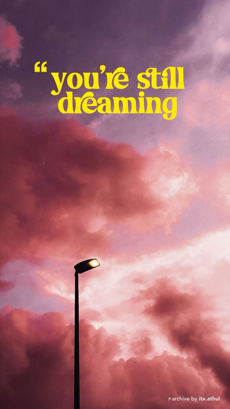 "You're still dreaming" in yellow type over pink storm clouds with a street lamp.