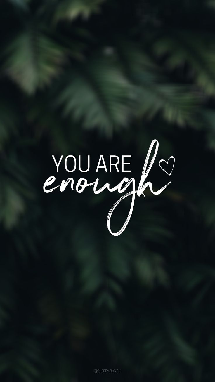 "You are enough" in white type and script over blurred dark green leaves.