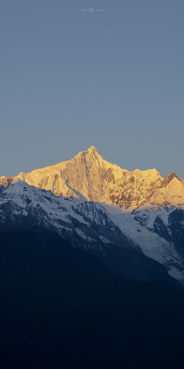 A golden-lit snowy mountain peak above dark blue slopes.