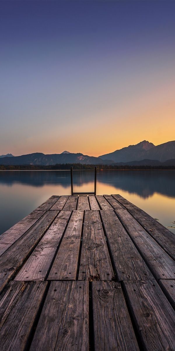 Weathered boards of a lakeside dock in the foreground, with calm water and dark hills at dusk.
