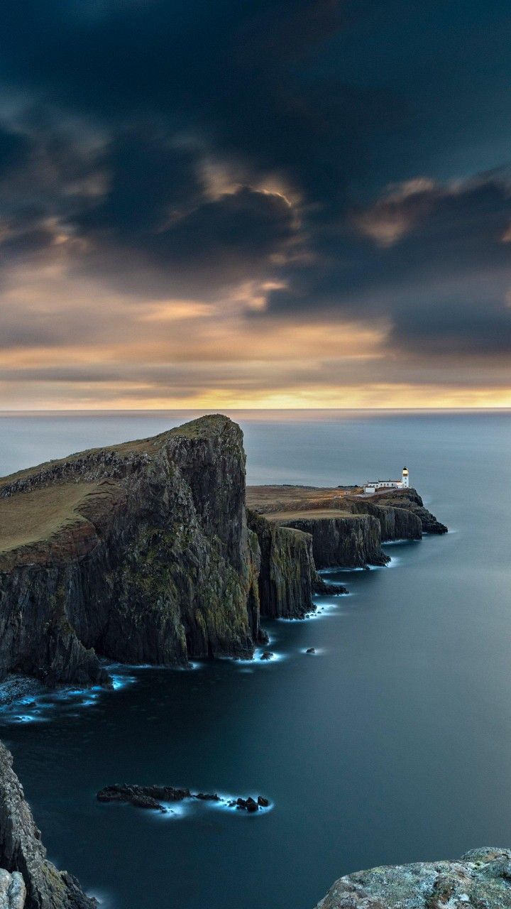 A lighthouse headland jutting into the sea beneath dramatic clouds at dusk.