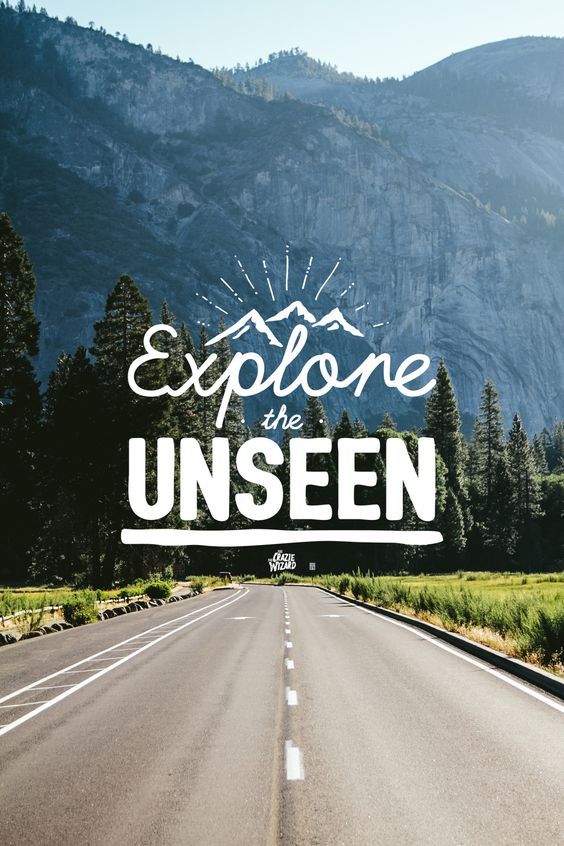 "Explore the unseen" in white over an empty road heading into forested mountains.