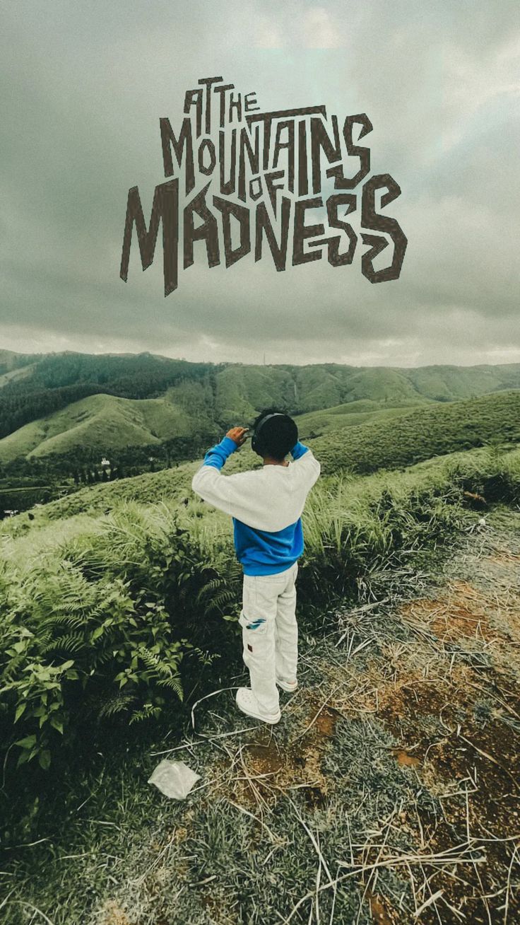 "Mountains of madness" in grey lettering above a person photographing a green valley.