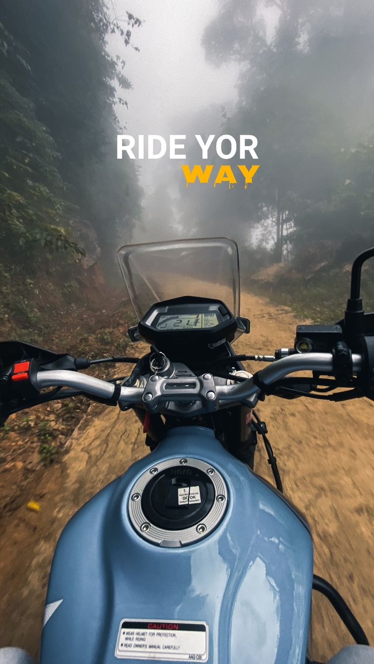 "Ride your way" in white and yellow above the fuel tank of a motorcycle on a misty trail.