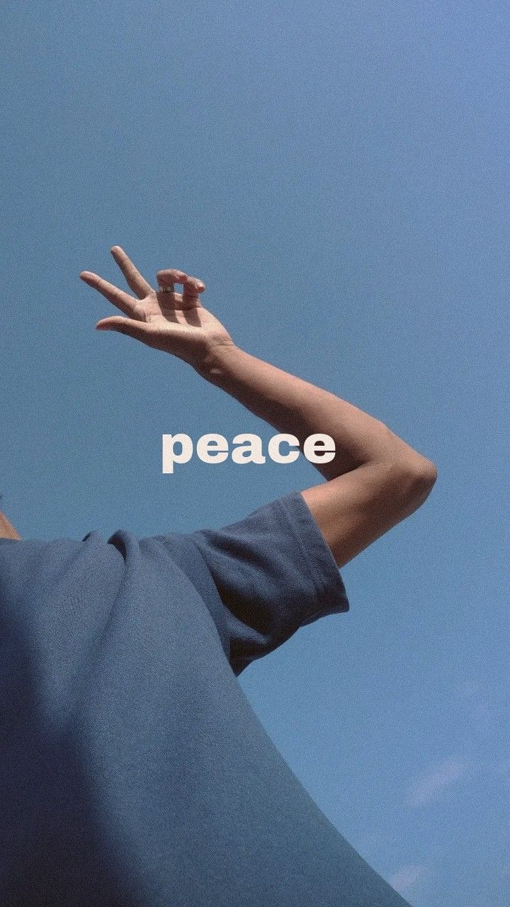 A hand making a peace sign against a blue sky with the word "Peace".