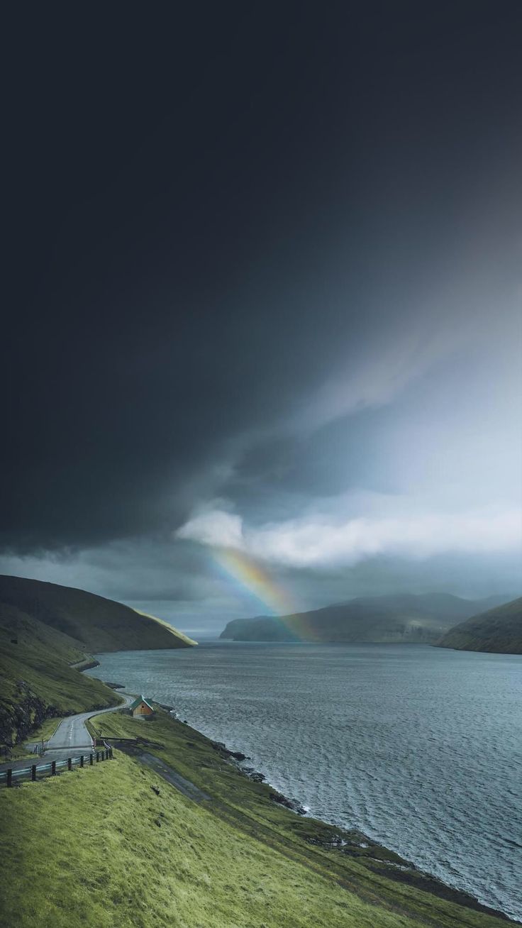 A faint rainbow over a dark coastal inlet under heavy grey clouds.
