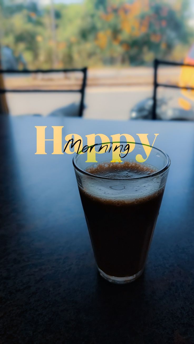 A glass of black coffee on a table with "Happy morning" in yellow lettering.
