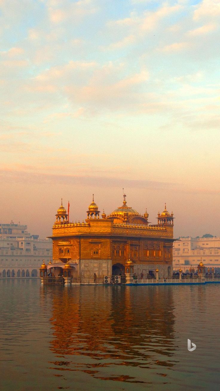 The Golden Temple in Amritsar reflected in its sacred pool under a warm hazy sky.