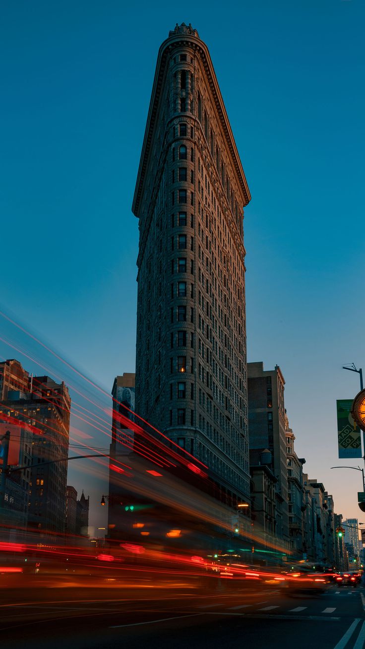 The Flatiron Building towering over a city street streaked with car light trails.