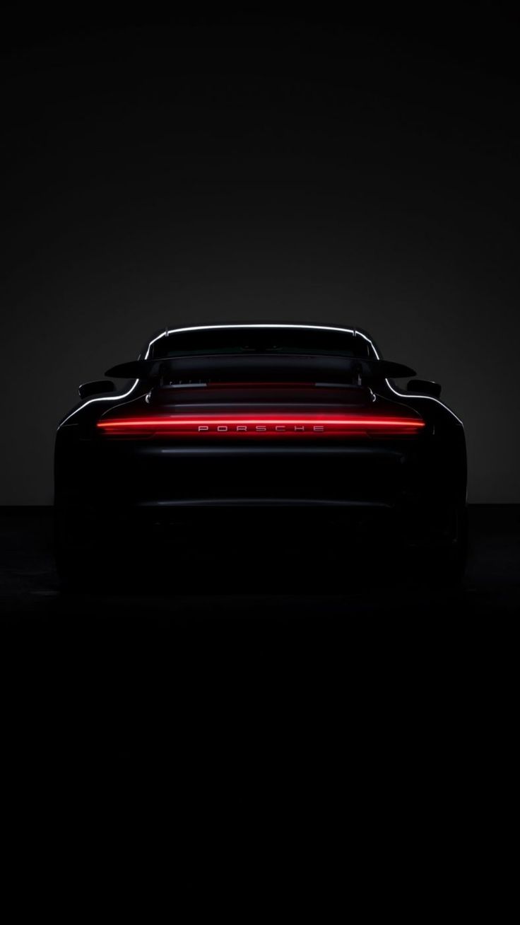 The thin glowing red tail light of a black sports car in darkness.