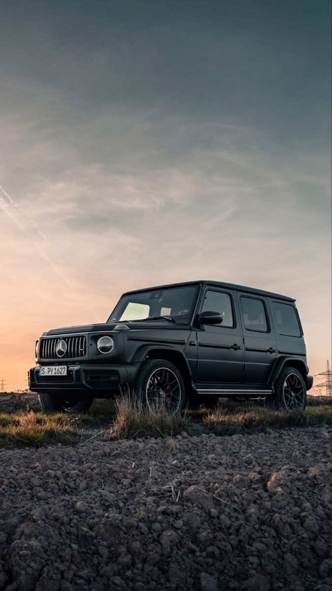 A black Mercedes G-Class on gravel under a cloudy sunset sky.