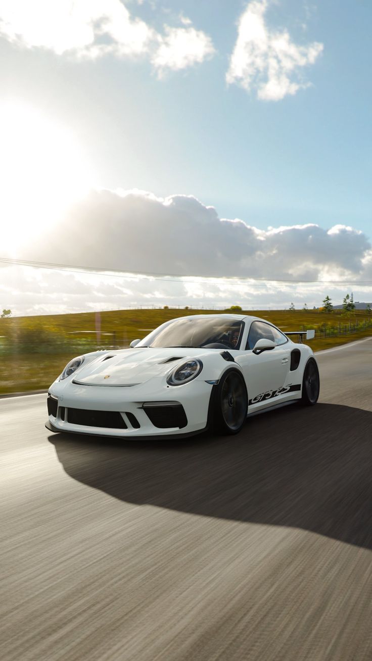 A white Porsche 911 GT3 speeding along a road under a sunny sky.