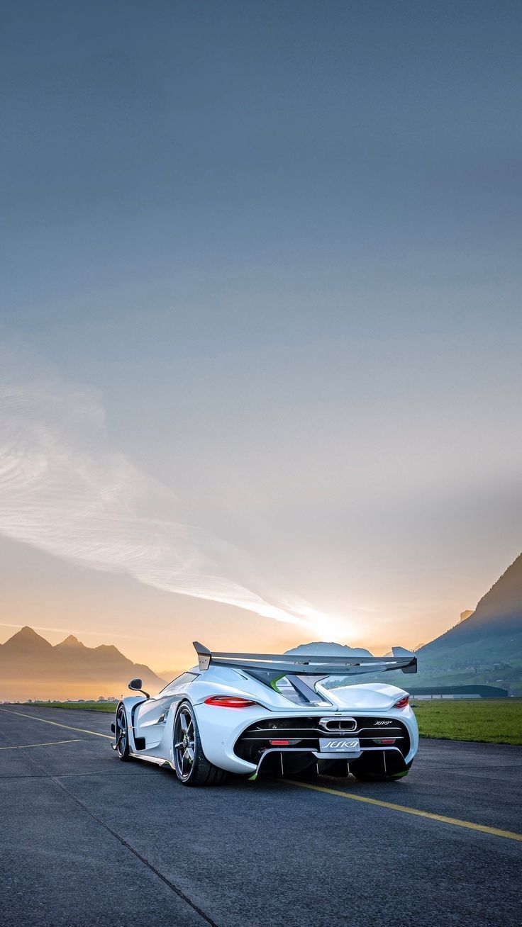 A white hypercar driving toward the camera on an open road at sunset.