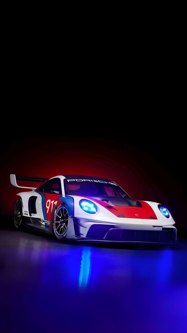 A red and white Porsche race car glowing under blue lights on a black background.