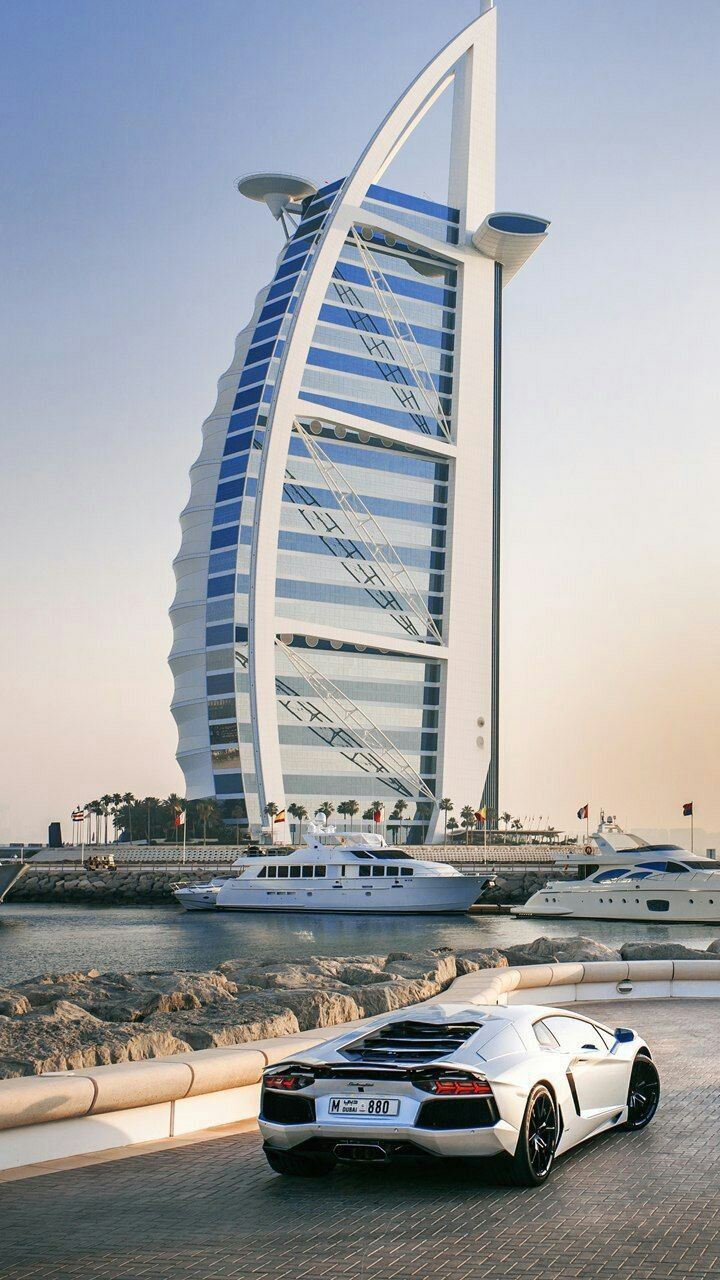 The Burj Al Arab hotel in Dubai with a white Lamborghini parked in front.
