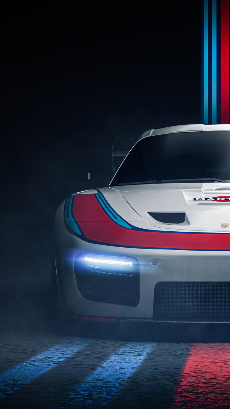 The front of a white Porsche race car with red and blue stripes in dark studio light.