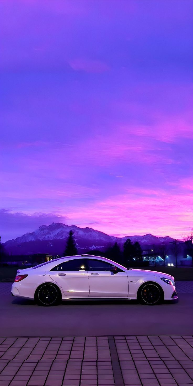 A white Mercedes CLS parked on a brick plaza under a vivid purple sky with mountains.