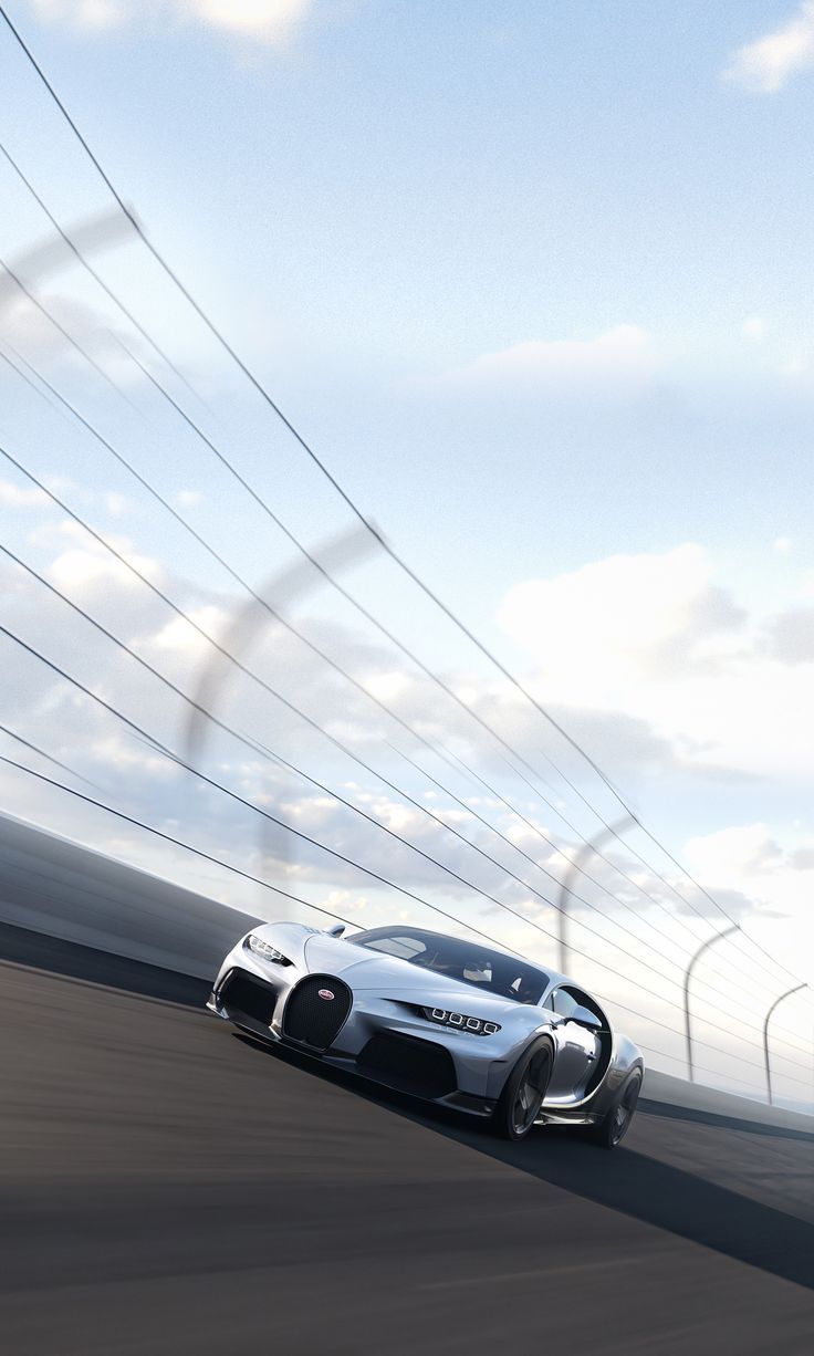 A white Bugatti Chiron speeding round a curved road under a blue sky.