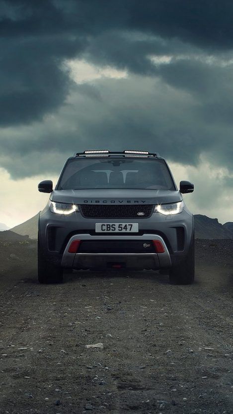 A grey Land Rover Discovery on a gravel track under dark storm clouds.