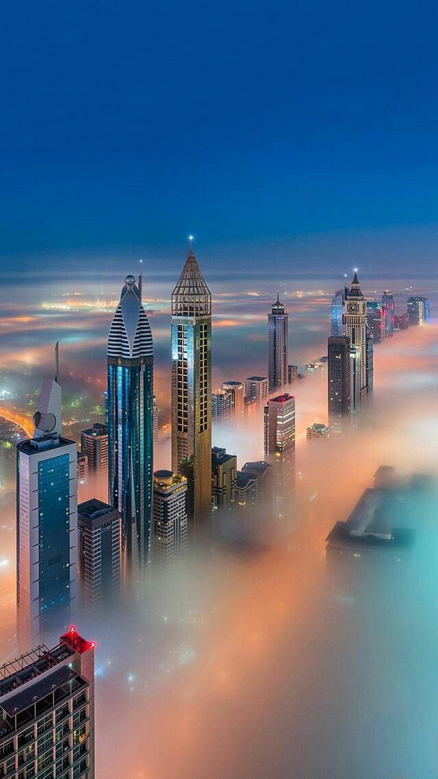 Futuristic skyscrapers rising above a sea of fog under a deep blue sky.