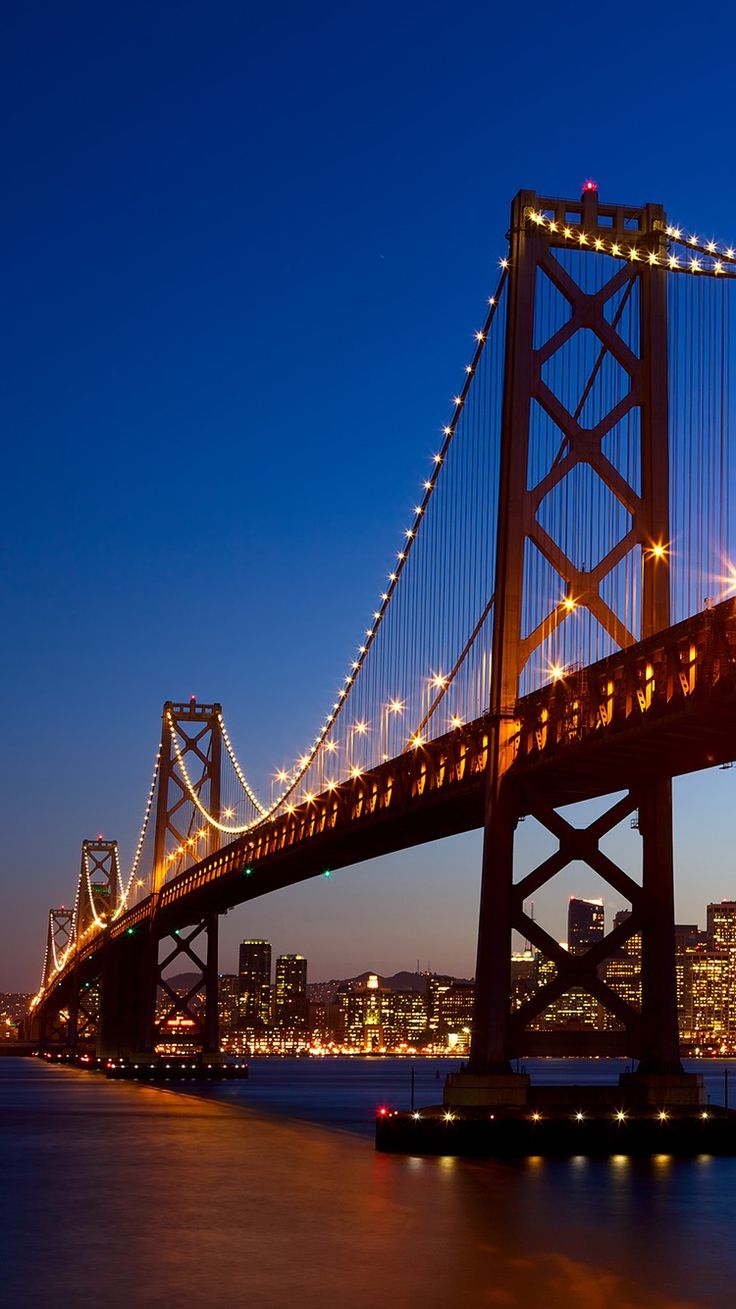 The San Francisco Bay Bridge lit up against a deep blue night sky.