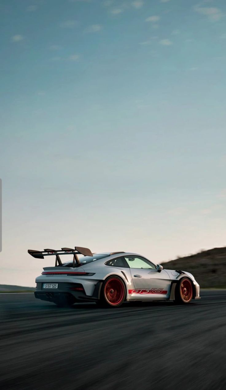 A white Porsche 911 GT3 RS on a road with hills behind at dusk.