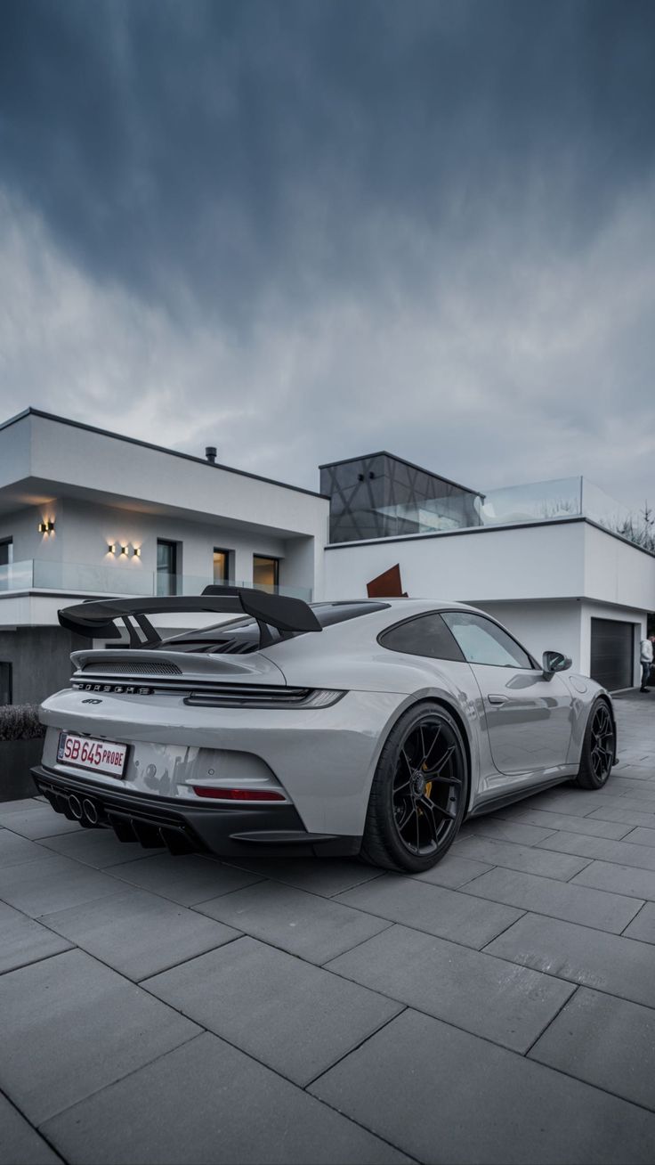 A grey Porsche 911 parked outside a modern white house.