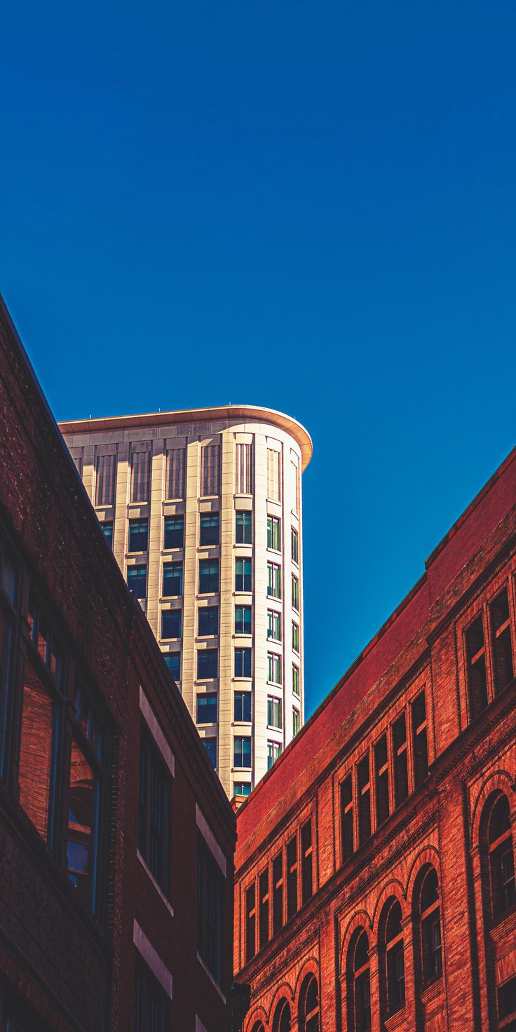 Looking up at a curved glass tower above red brick buildings under a blue sky.