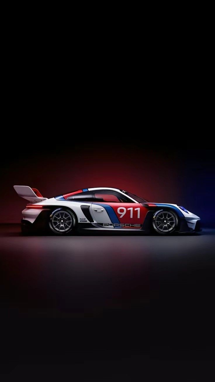 A white and red Porsche 911 race car in dark studio light.